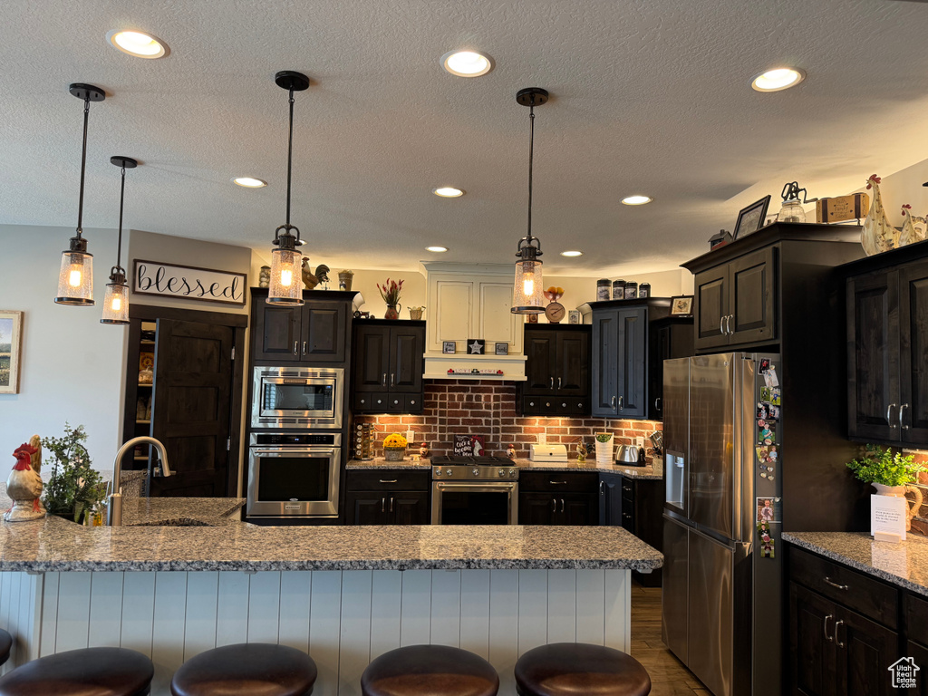 Kitchen featuring stainless steel appliances, a sink, a breakfast bar, decorative backsplash, and decorative light fixtures