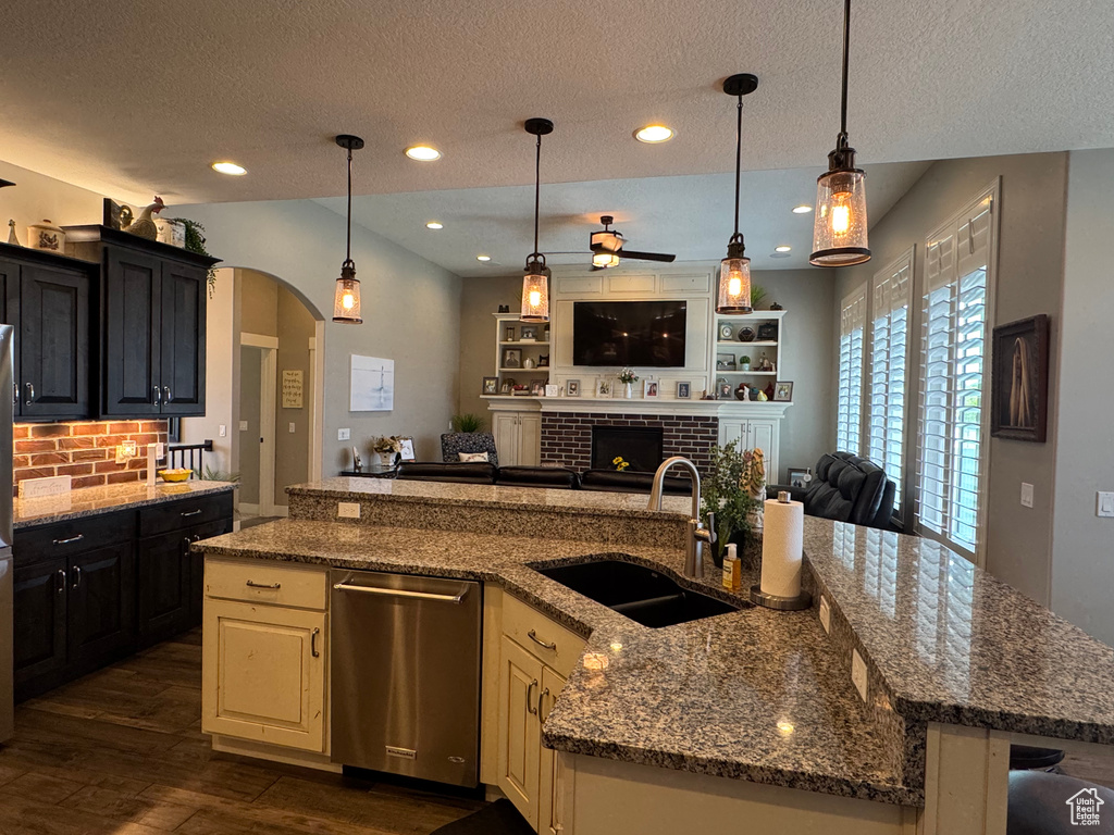 Kitchen featuring a sink, stainless steel dishwasher, open floor plan, a textured ceiling, and dark wood finished floors