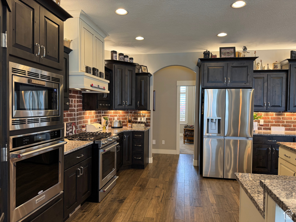 Kitchen featuring stainless steel appliances, arched walkways, decorative backsplash, light stone countertops, and recessed lighting