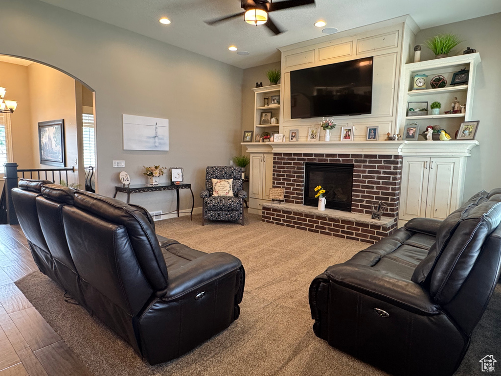 Living room with a ceiling fan, arched walkways, a chandelier, a fireplace, and recessed lighting