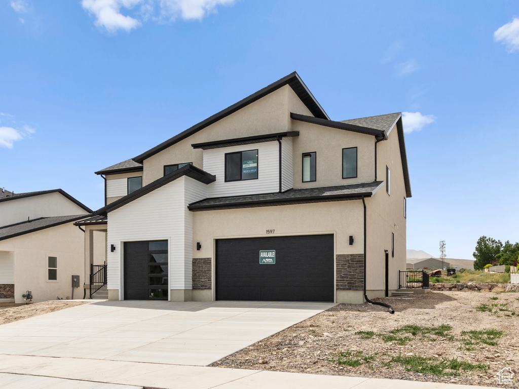 Modern home with driveway, stucco siding, an attached garage, and stone siding
