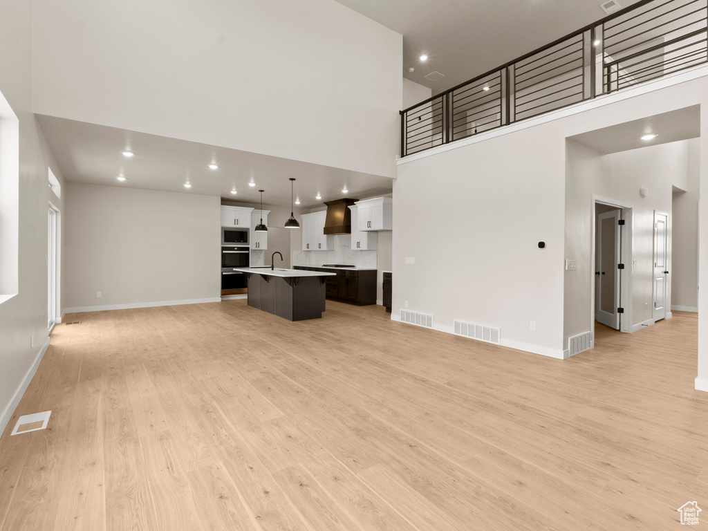 Unfurnished living room with a high ceiling, light wood-style flooring, and recessed lighting