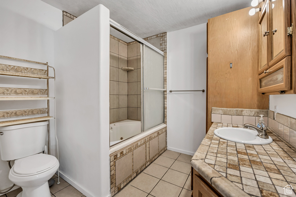 Bathroom featuring toilet, vanity, tile patterned flooring, tiled shower / bath combo, and baseboards