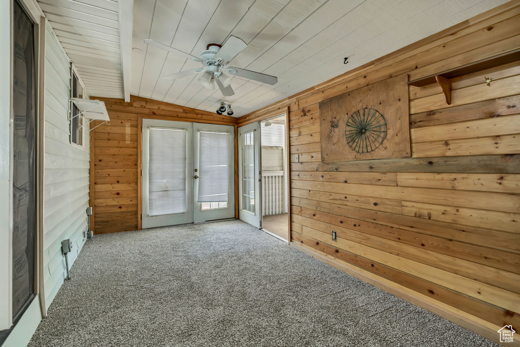 Empty room with french doors, wood walls, carpet floors, ceiling fan, and lofted ceiling