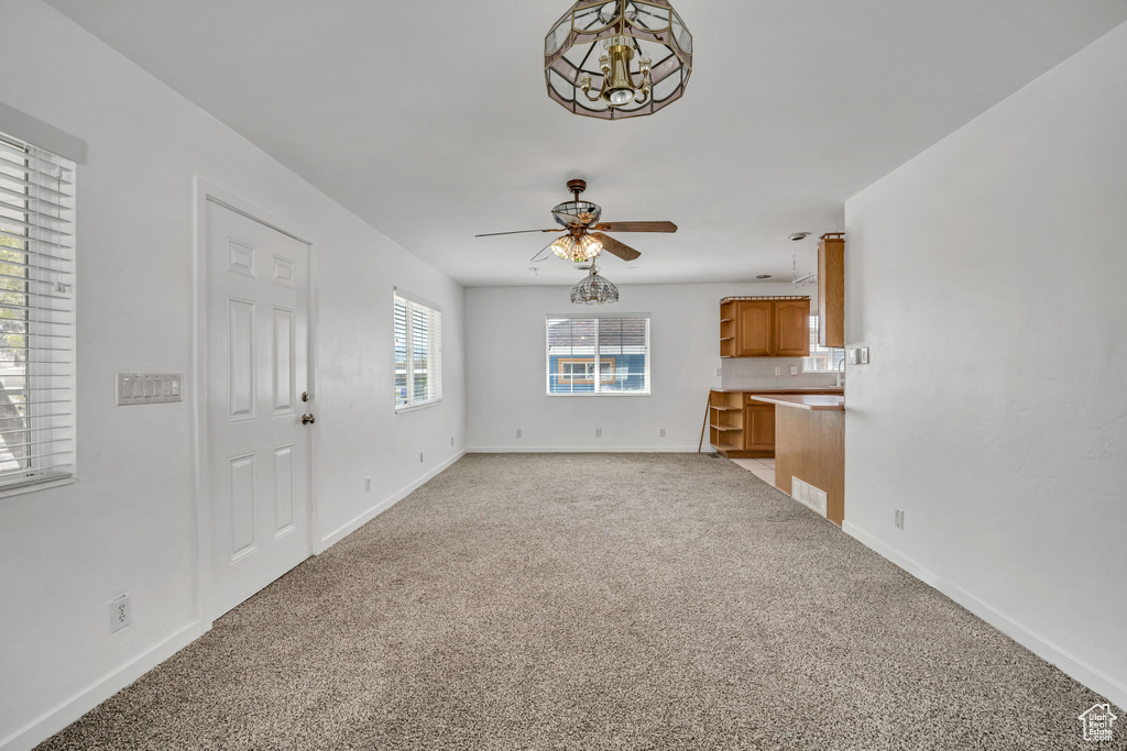 Unfurnished living room featuring light colored carpet, ceiling fan, baseboards, and a chandelier