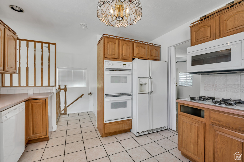 Kitchen featuring white appliances, backsplash, a chandelier, and light countertops