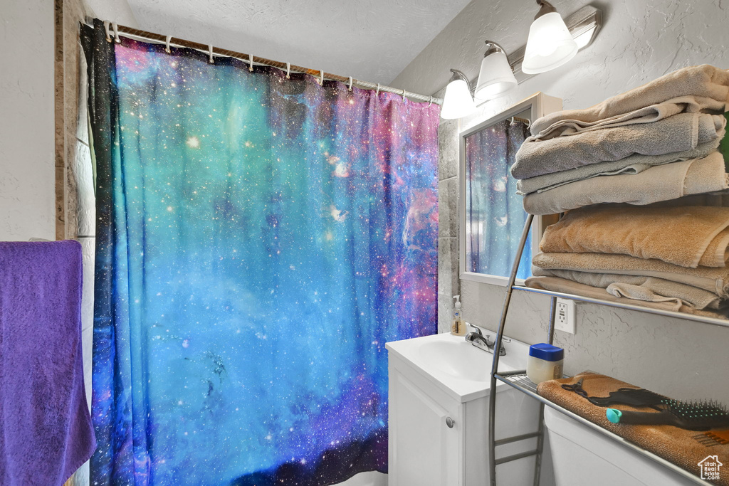 Bathroom with a textured wall, vanity, curtained shower, and a textured ceiling