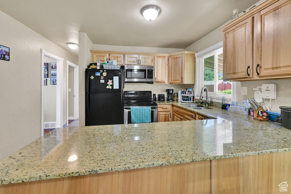 Kitchen with stainless steel appliances, a sink, light stone countertops, and light brown cabinetry