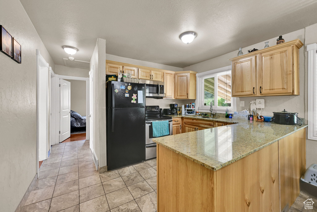 Kitchen with stainless steel appliances, a peninsula, a sink, light brown cabinets, and light stone countertops