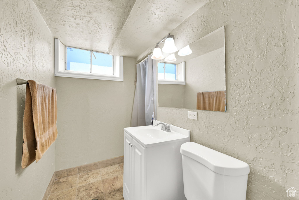 Bathroom with a textured wall, a textured ceiling, vanity, toilet, and stone finish floors