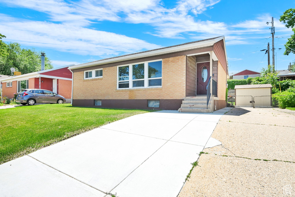 View of front facade with brick siding, a front yard, driveway, and a gate