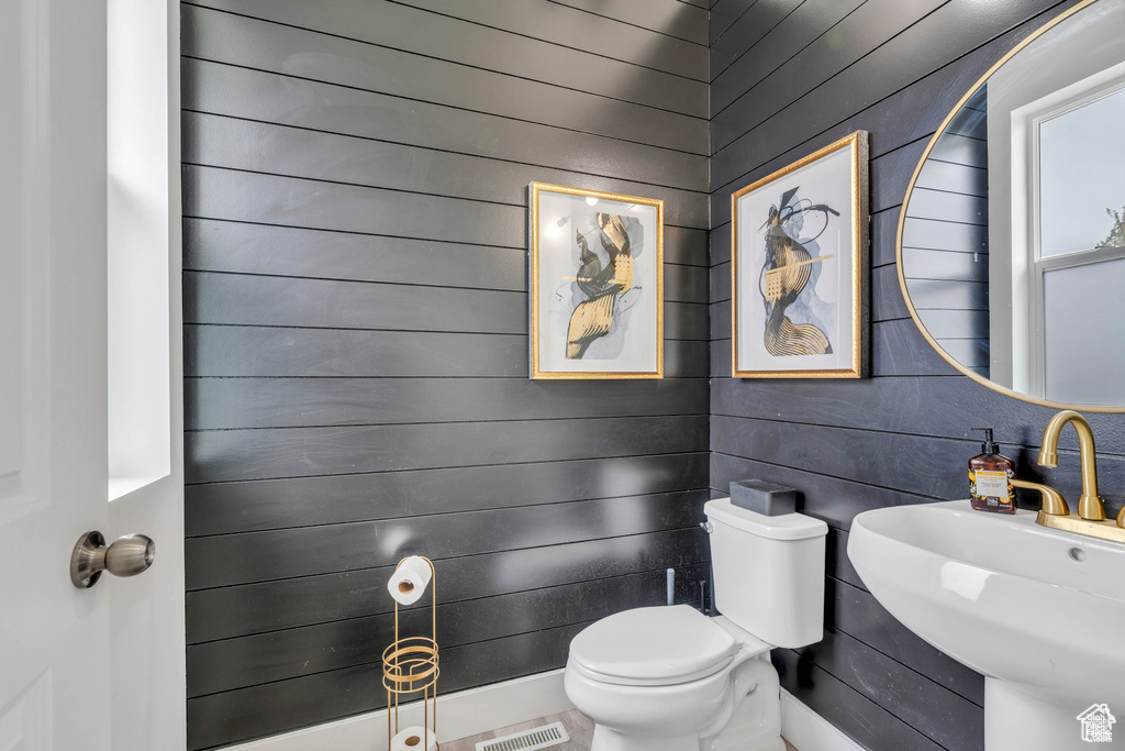 Half bath featuring toilet, a sink, and wooden walls