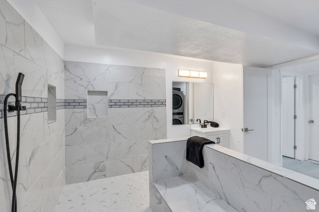 Bathroom with stacked washing machine and dryer, a walk in shower, and vanity