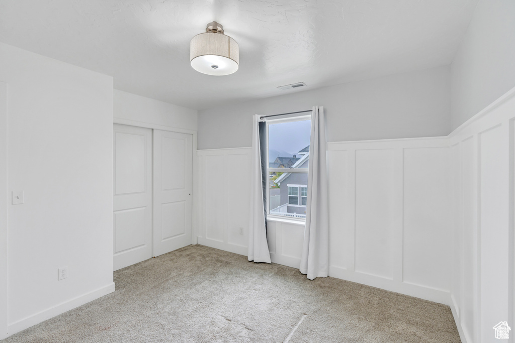 Unfurnished bedroom with carpet, a wainscoted wall, a decorative wall, and a closet