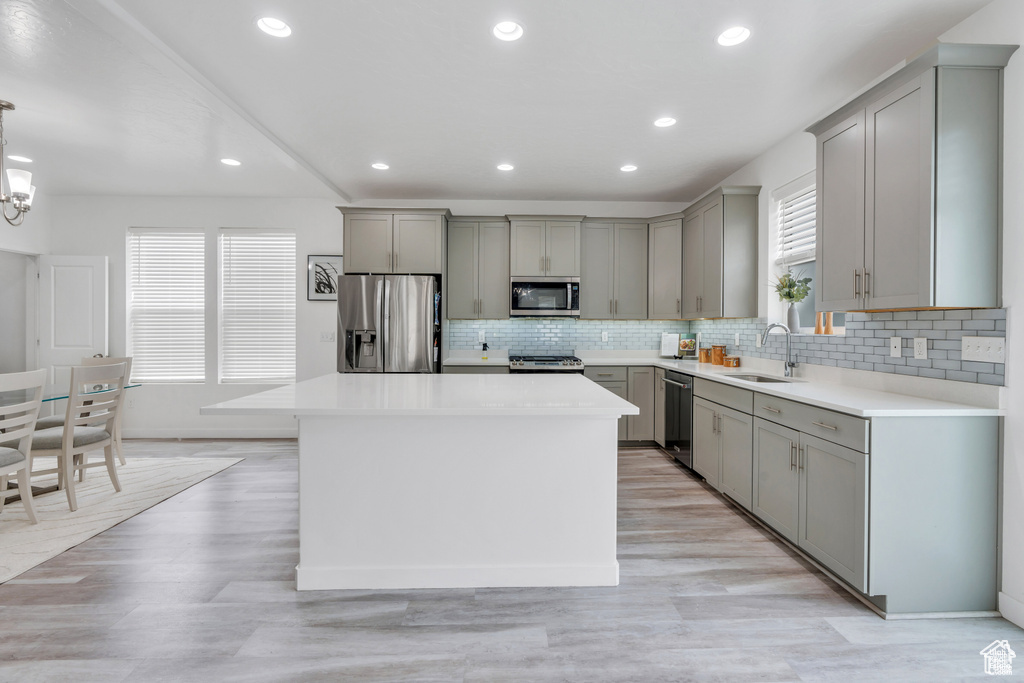 Kitchen with appliances with stainless steel finishes, gray cabinets, a sink, decorative backsplash, and a kitchen island