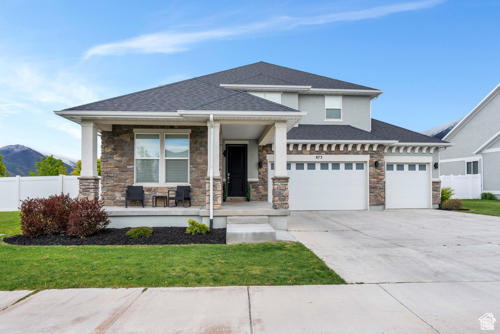 Prairie-style house with a porch, stone siding, concrete driveway, a shingled roof, and a garage