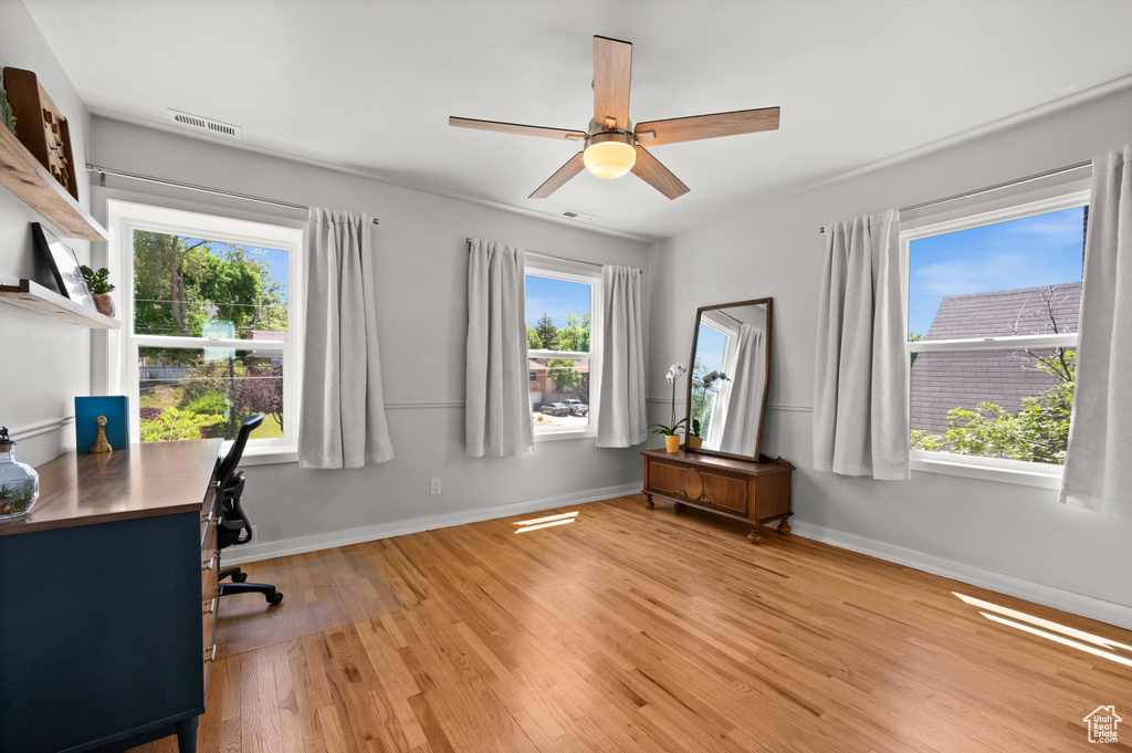 Unfurnished office with light wood-style floors, plenty of natural light, a ceiling fan, and baseboards