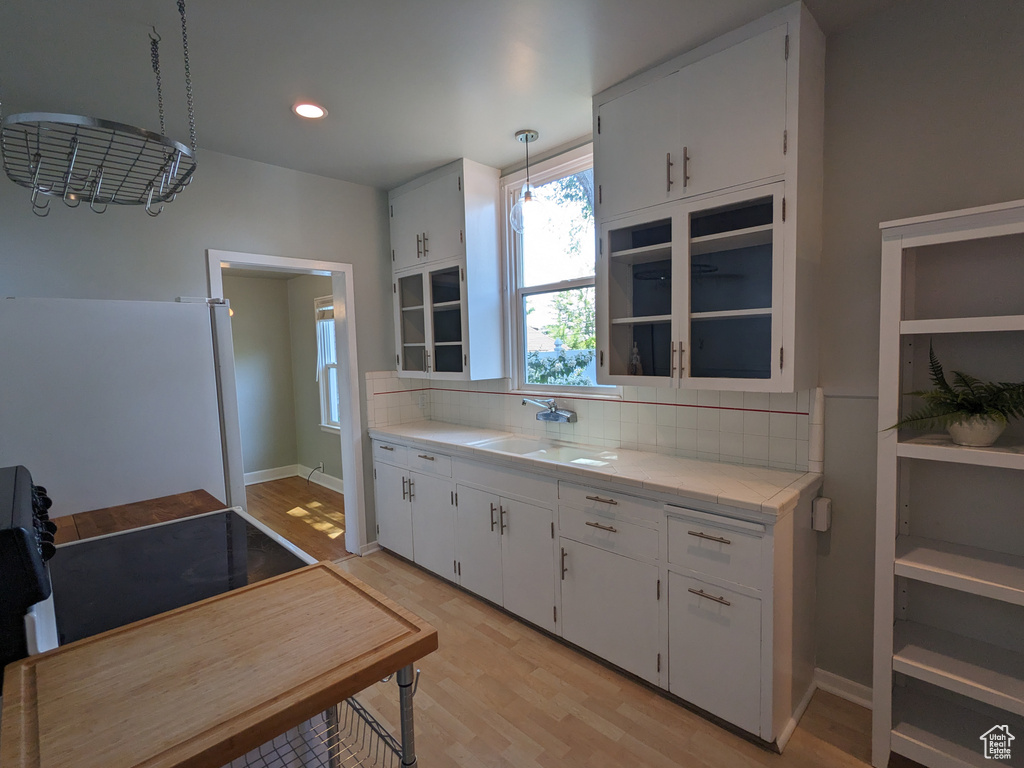 Kitchen with light countertops, a sink, decorative backsplash, light wood finished floors, and white cabinets