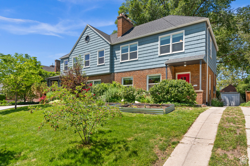 View of front of home featuring a chimney, a front yard, a garden, brick siding, and a shingled roof