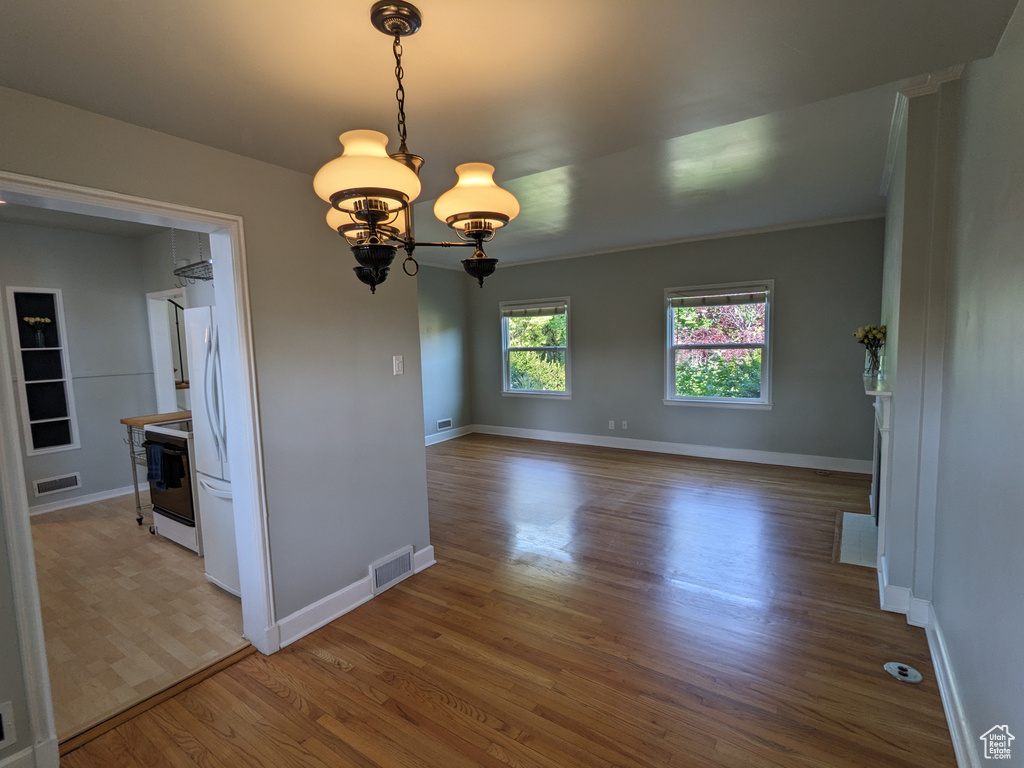 Spare room featuring wood finished floors, a chandelier, and baseboards