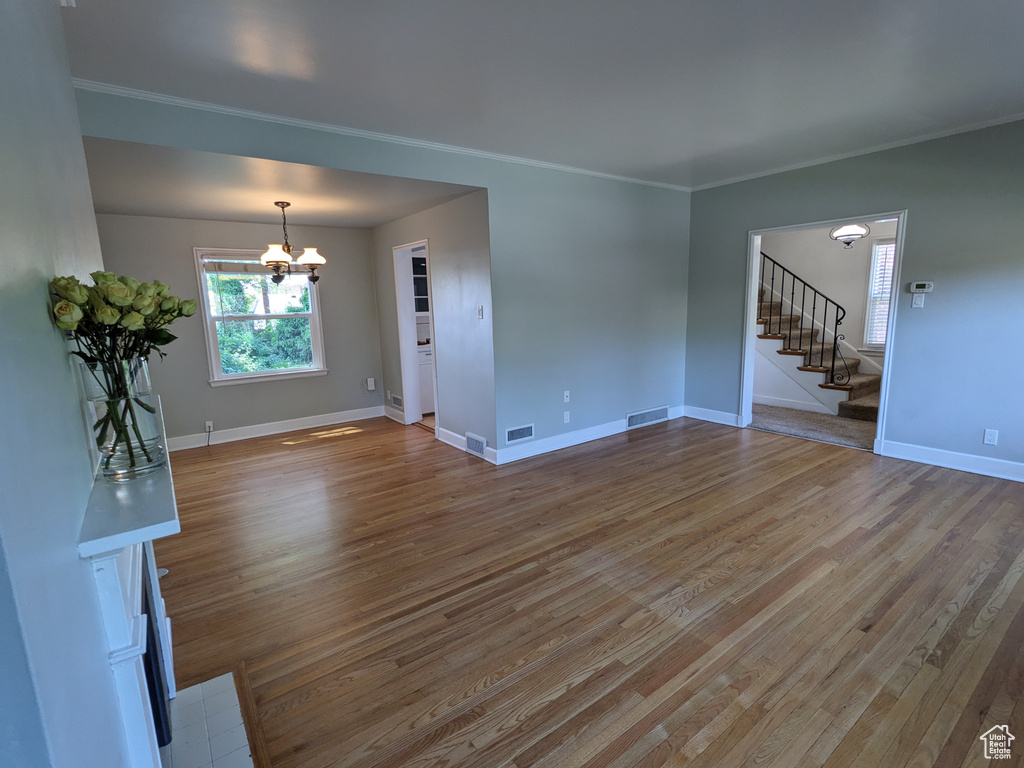 Unfurnished living room featuring stairs, a chandelier, light wood-style flooring, and ornamental molding