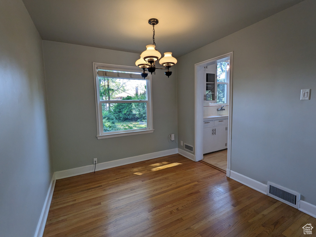 Spare room with a chandelier, light wood finished floors, and baseboards