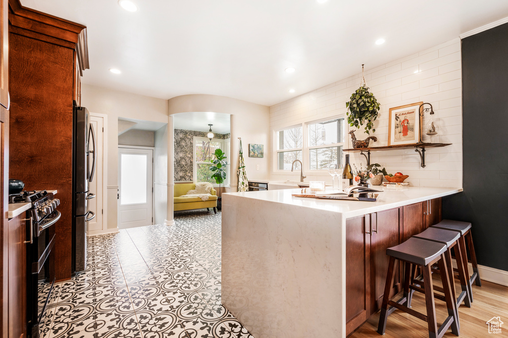 Kitchen featuring range with gas stovetop, freestanding refrigerator, a peninsula, a kitchen breakfast bar, and light countertops