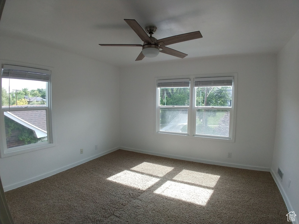 Carpeted spare room with plenty of natural light, a ceiling fan, and baseboards