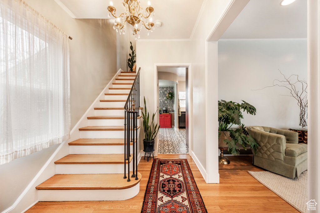 Foyer entrance featuring stairway, wood finished floors, a chandelier, crown molding, and baseboards