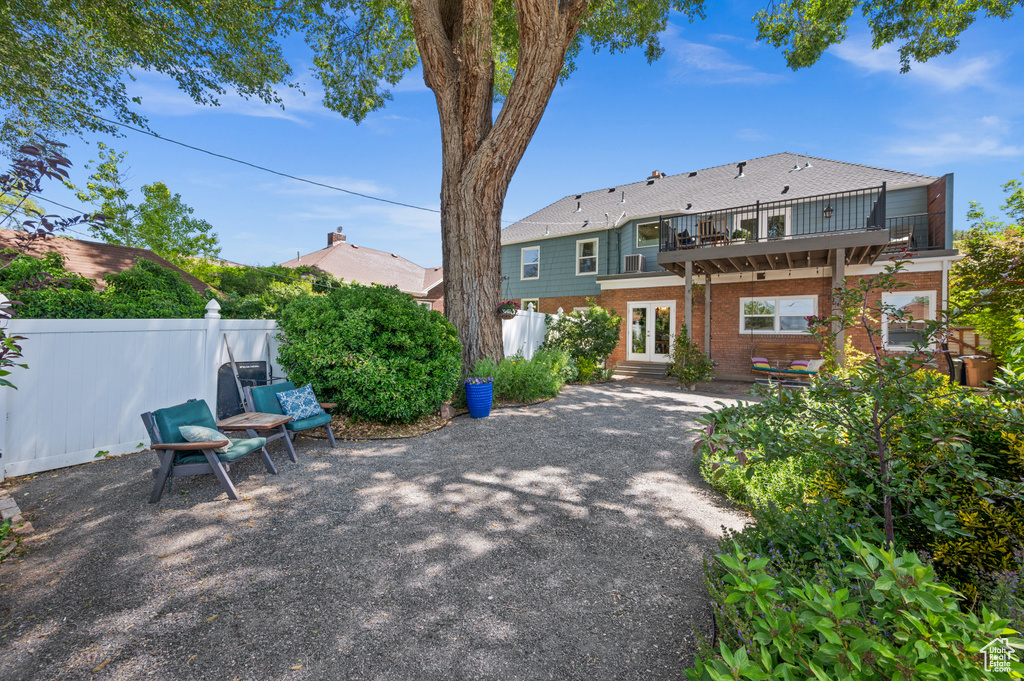 Back of house with a balcony, brick siding, french doors, and a patio