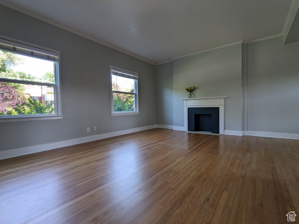 Unfurnished living room featuring wood finished floors, crown molding, a fireplace with flush hearth, and baseboards