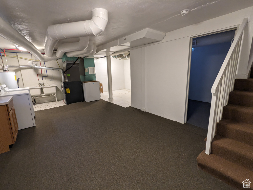 Finished basement featuring gas water heater, stairway, heating unit, and washer and clothes dryer