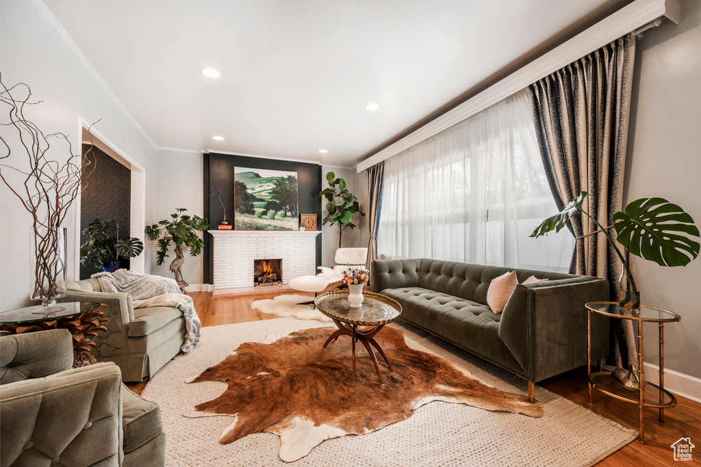 Living room featuring baseboards, wood finished floors, a brick fireplace, recessed lighting, and ornamental molding
