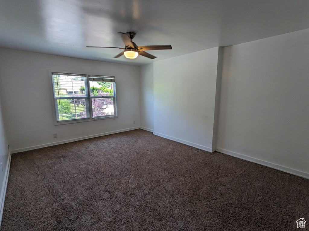Unfurnished room with ceiling fan, baseboards, and dark colored carpet