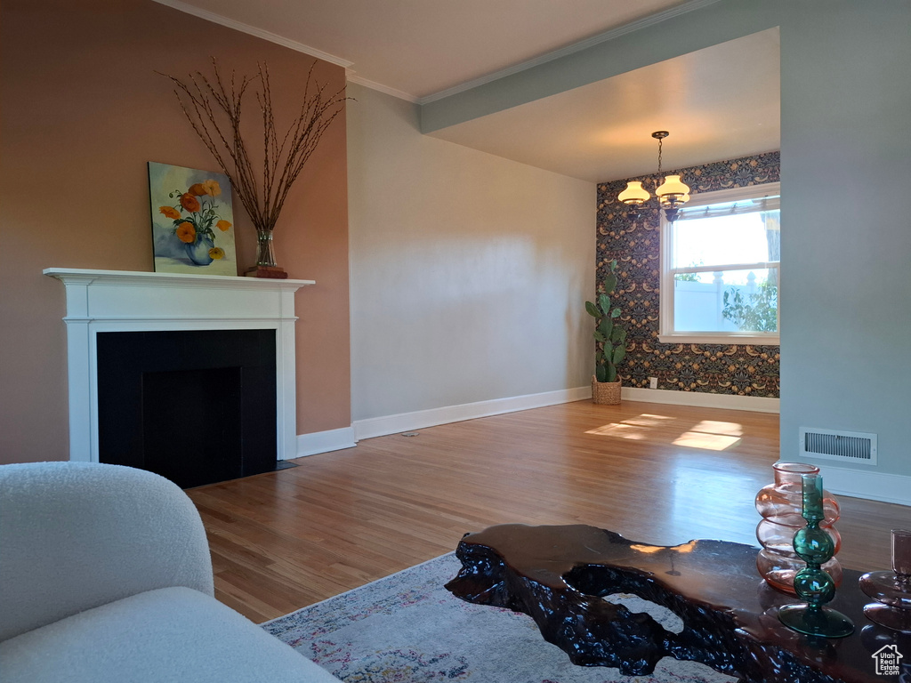 Living room featuring a chandelier, wood finished floors, ornamental molding, and a fireplace with flush hearth