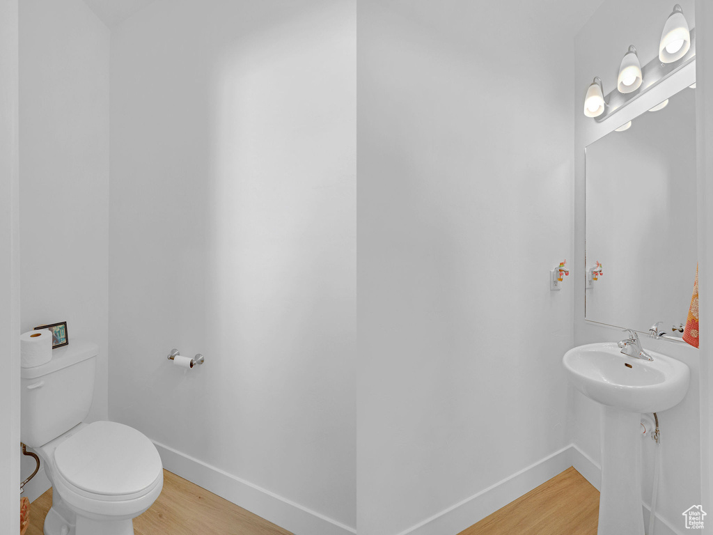 Half bathroom with wood finished floors, baseboards, and toilet