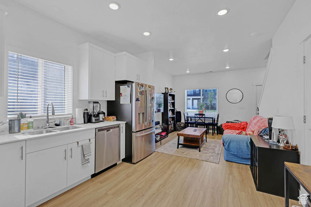 Kitchen with appliances with stainless steel finishes, a sink, light wood-style floors, light countertops, and white cabinets