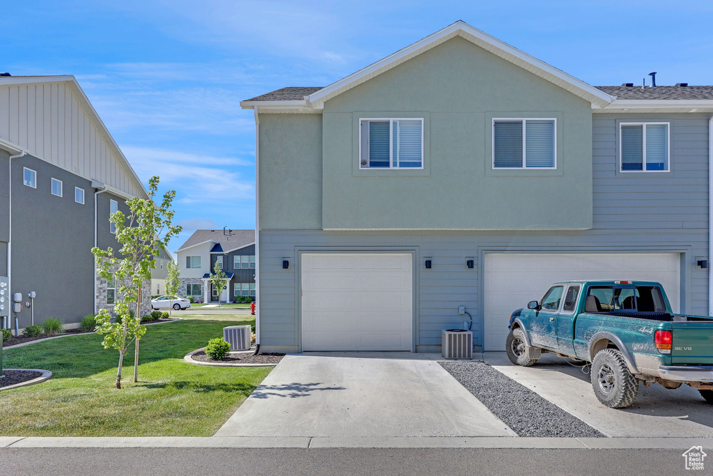 View of front of home featuring driveway, a front lawn, central AC, and a garage