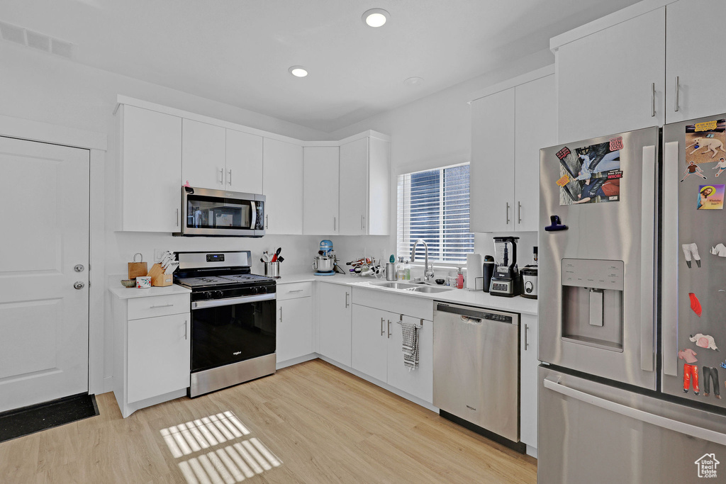 Kitchen with appliances with stainless steel finishes, a sink, light wood-style floors, light countertops, and white cabinetry
