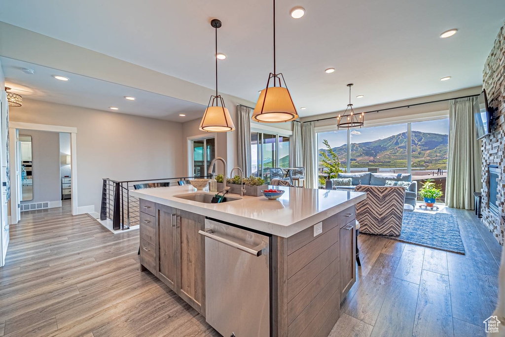 Kitchen with a sink, dishwasher, light wood-style floors, a kitchen island with sink, and light countertops
