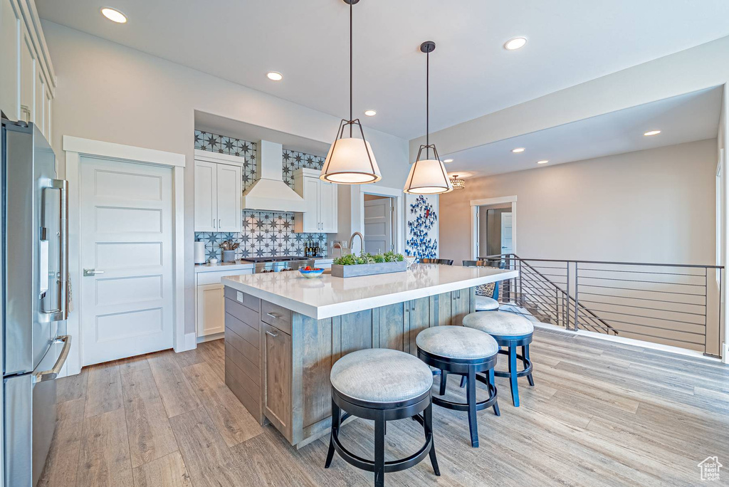 Kitchen featuring custom exhaust hood, high end refrigerator, light wood-style flooring, a breakfast bar, and recessed lighting