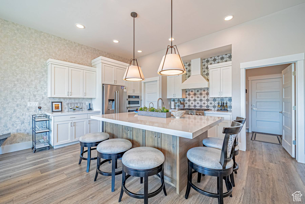 Kitchen with custom exhaust hood, appliances with stainless steel finishes, a breakfast bar area, white cabinets, and wallpapered walls