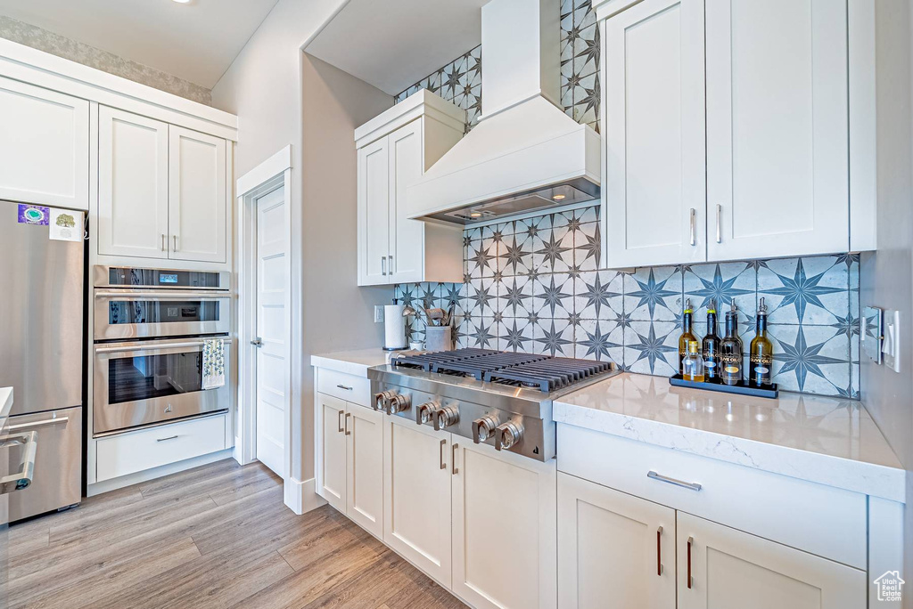 Kitchen featuring custom range hood, stainless steel appliances, tasteful backsplash, and white cabinets