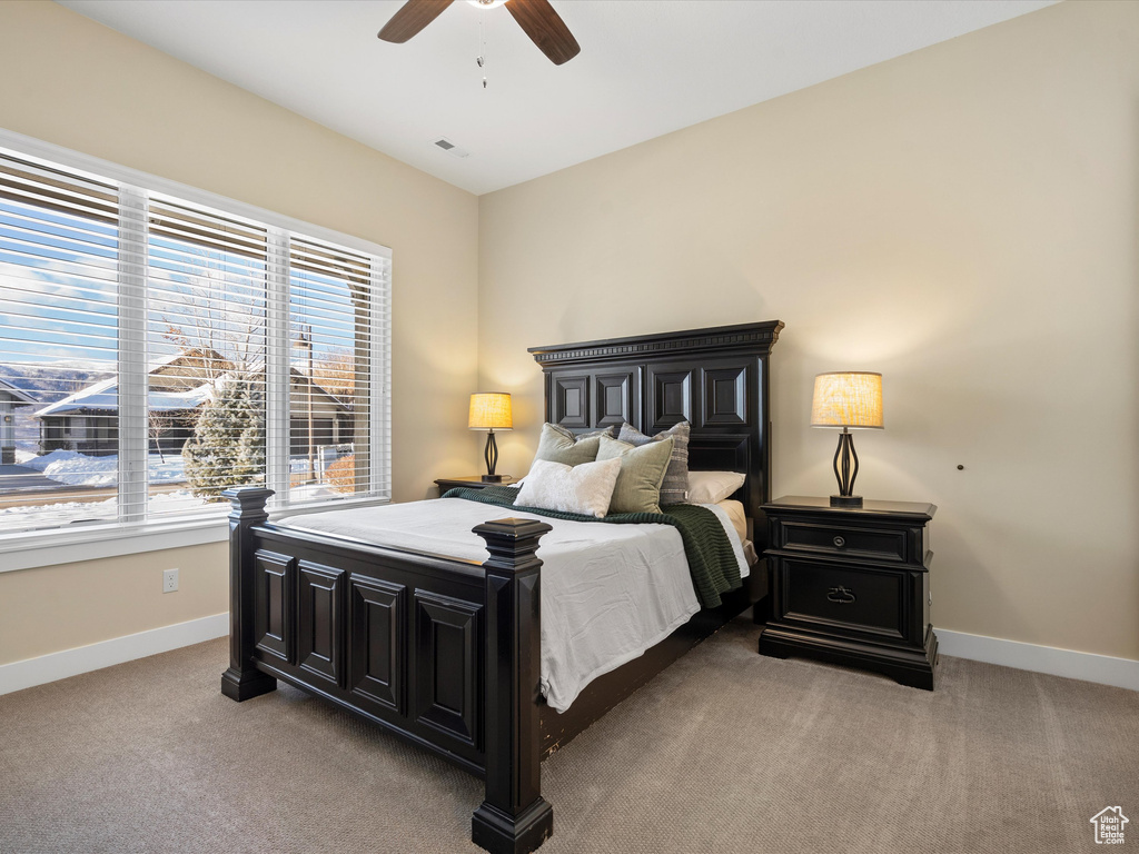 Bedroom featuring multiple windows, baseboards, light carpet, and a ceiling fan