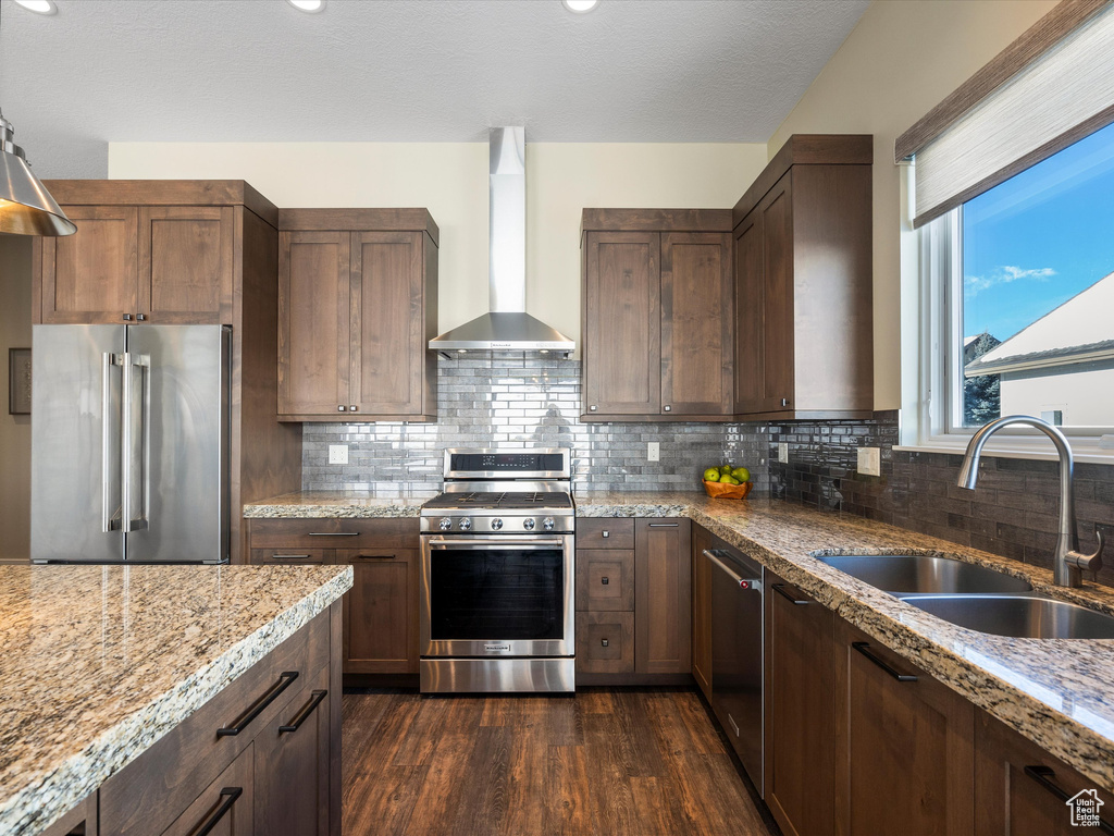 Kitchen with stainless steel appliances, wall chimney range hood, a sink, dark wood-style floors, and light stone counters