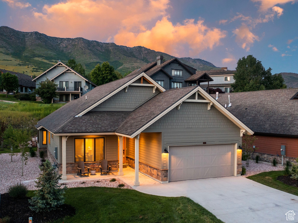 Craftsman house with stone siding, a garage, a mountain view, a porch, and concrete driveway