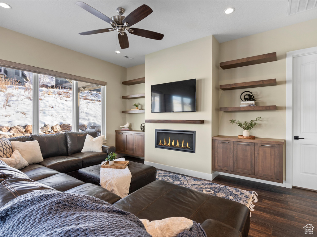 Living area with a glass covered fireplace, a ceiling fan, recessed lighting, dark wood-style flooring, and baseboards