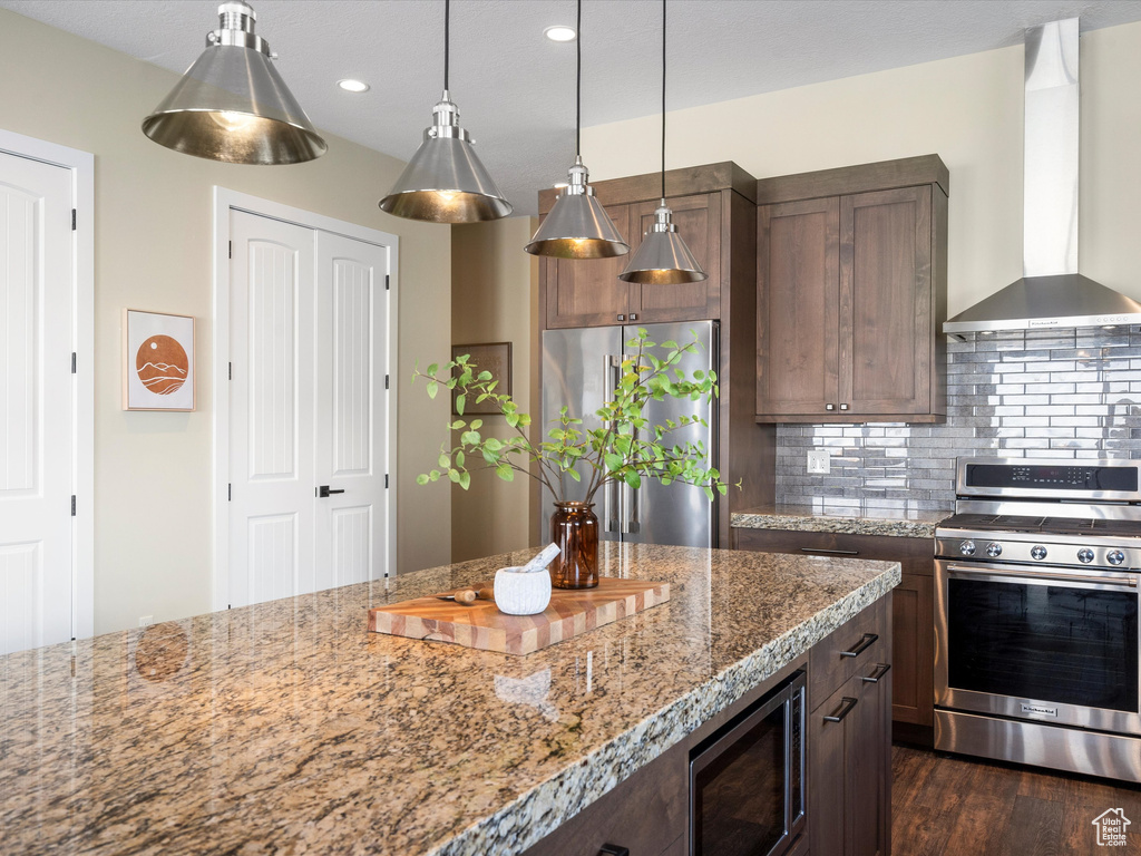 Kitchen with appliances with stainless steel finishes, wall chimney exhaust hood, tasteful backsplash, light stone countertops, and recessed lighting
