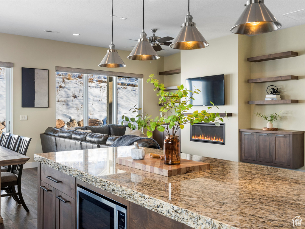 Kitchen with a glass covered fireplace, plenty of natural light, stainless steel microwave, hanging light fixtures, and recessed lighting