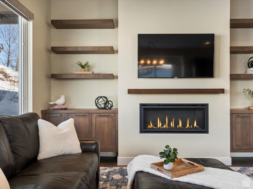 Living area with wood finished floors, a glass covered fireplace, built in features, and baseboards
